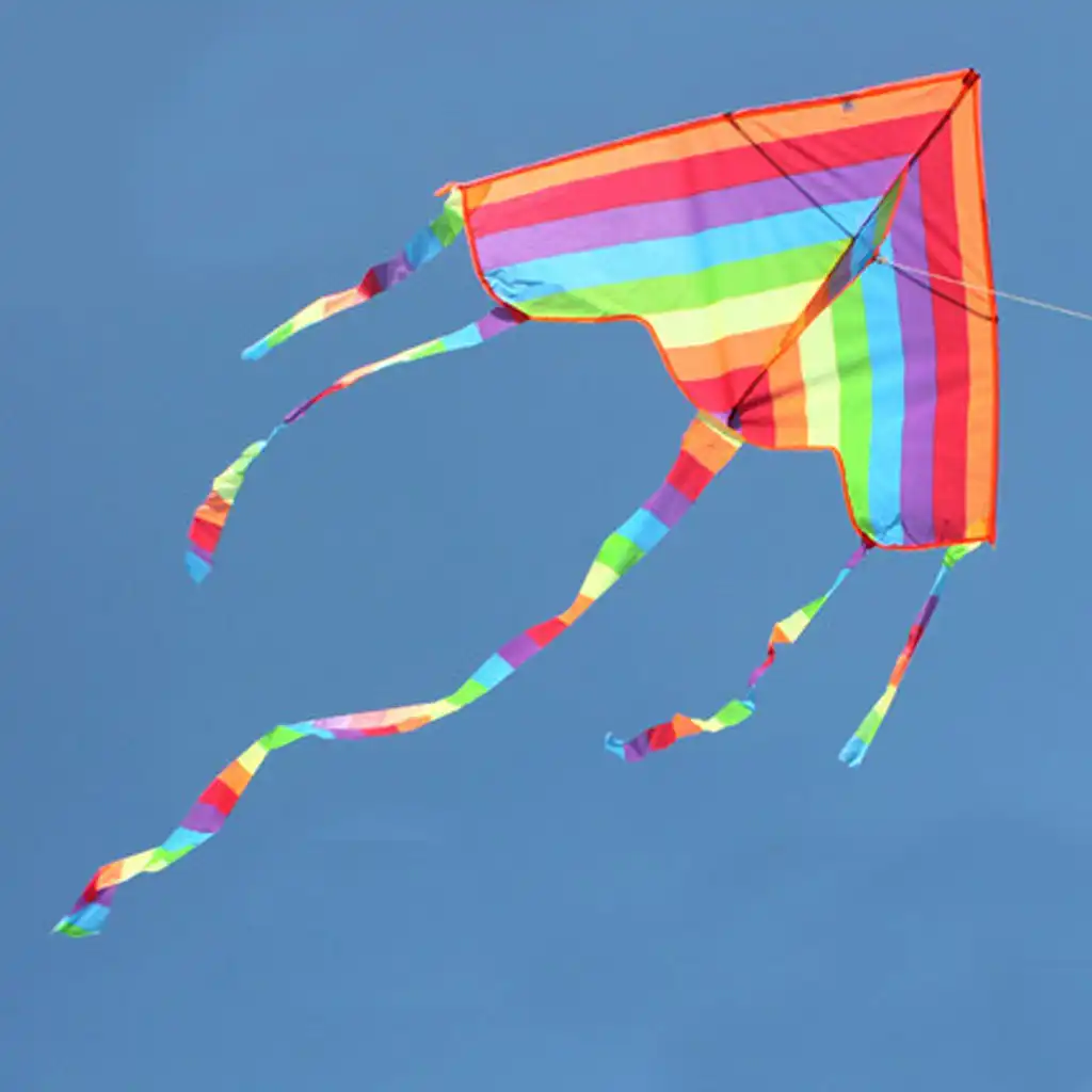 Action shot of rainbow triangle kite catching wind and lifting off from sandy beach surface.