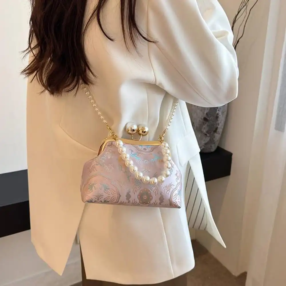 Chinese pearl embroidery clutch bag with kiss lock closure on elegant silk fabric background.