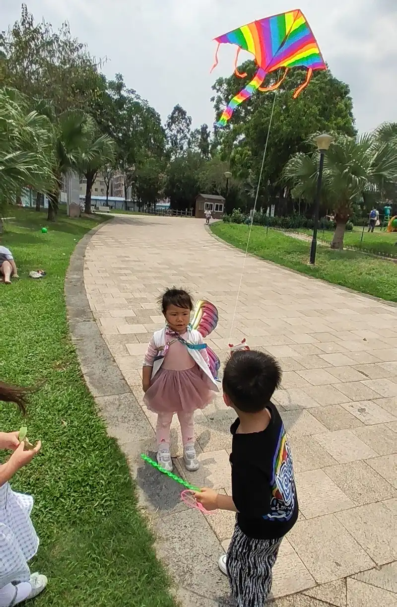 Colorful rainbow triangle kite flying high in blue sky with white clouds background.