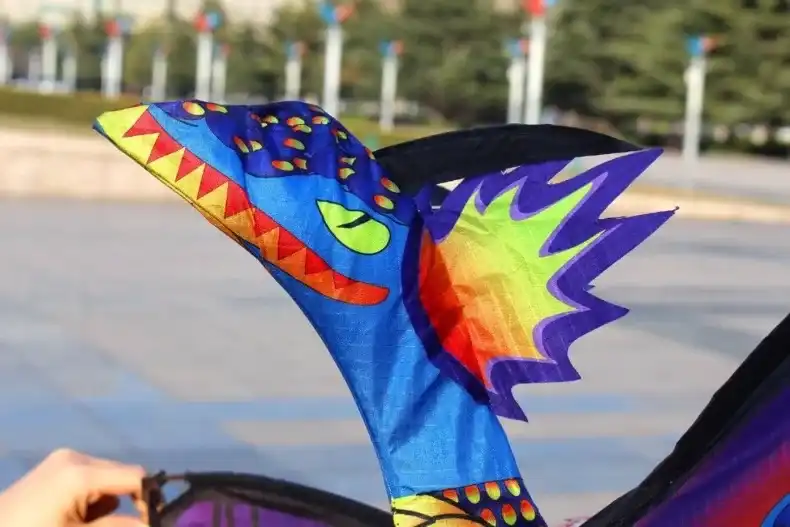 3D dragon kite flying at beach with adult controlling flight showing outdoor recreational activity.