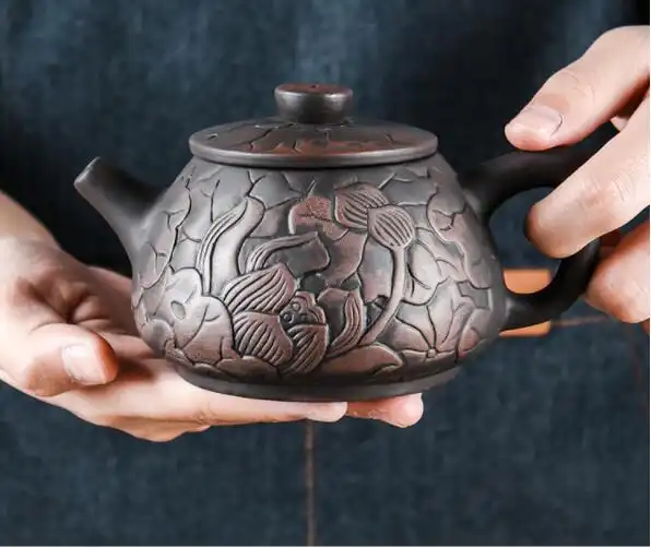 Hand carved lotus black mud Yixing teapot with intricate purple clay artistic illustration design.