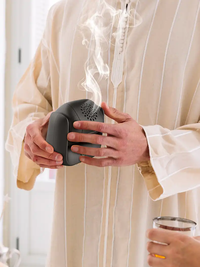 Hand holding compact rechargeable incense burner demonstrating portable size and ergonomic design.