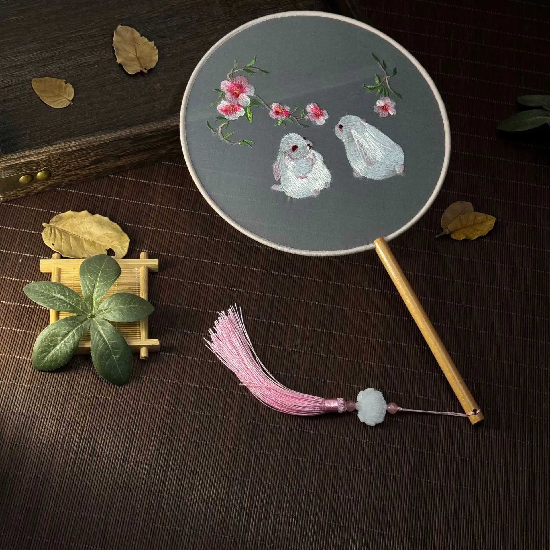 Traditional Chinese fan displayed open showing full embroidered design and tassel decoration.