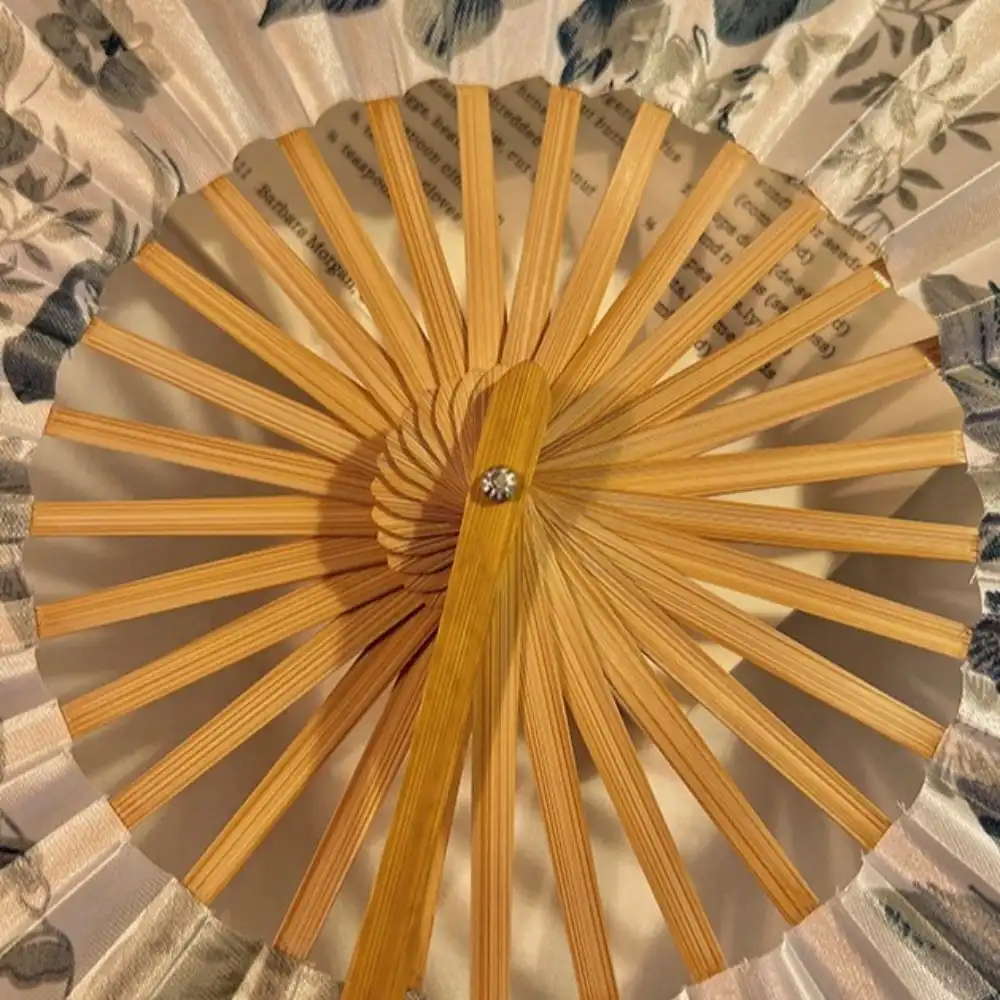 Female hand holding opened circular fan demonstrating proper grip and graceful usage posture for cooling.