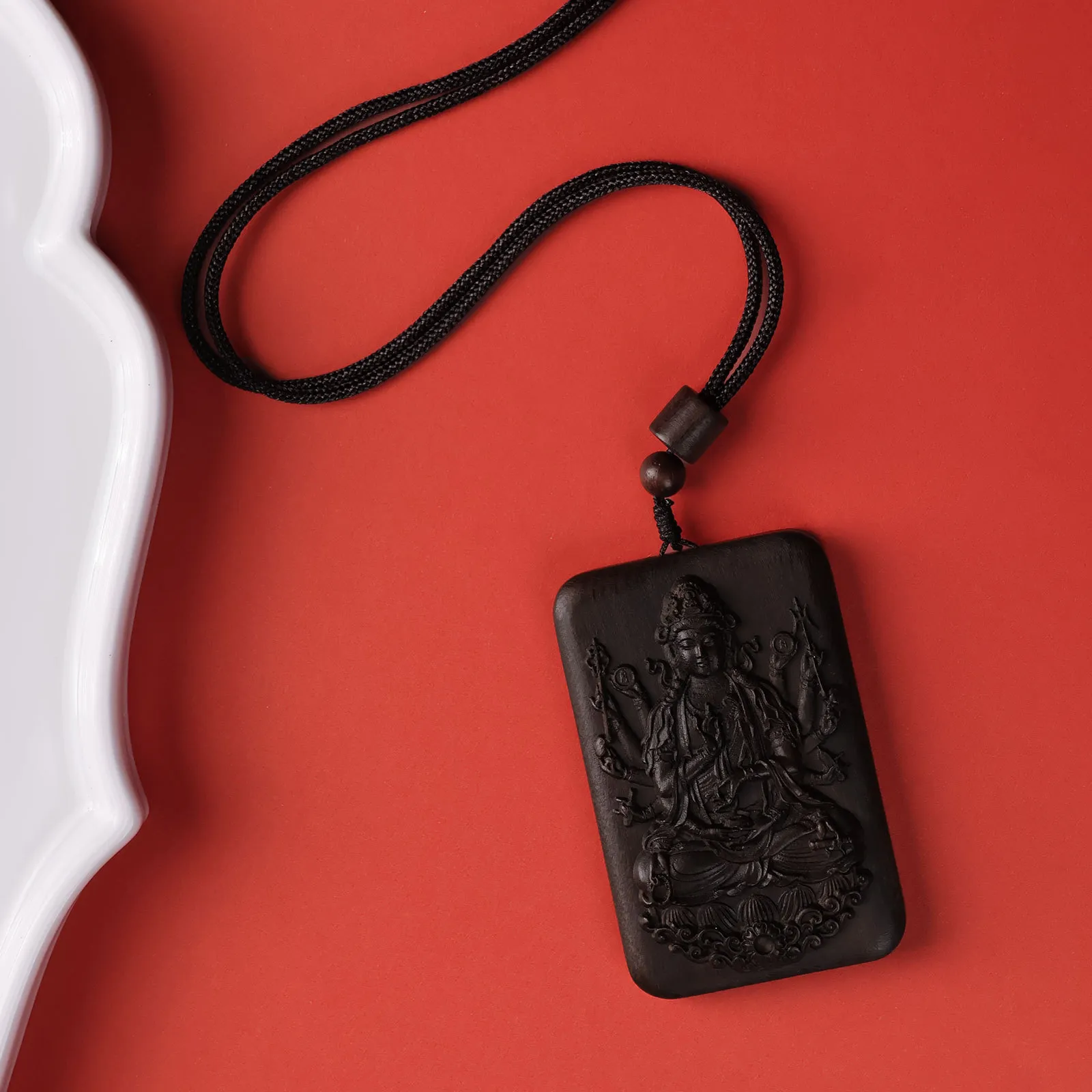Agarwood Guanyin pendant laying flat displaying intricate thousand hands carving details.