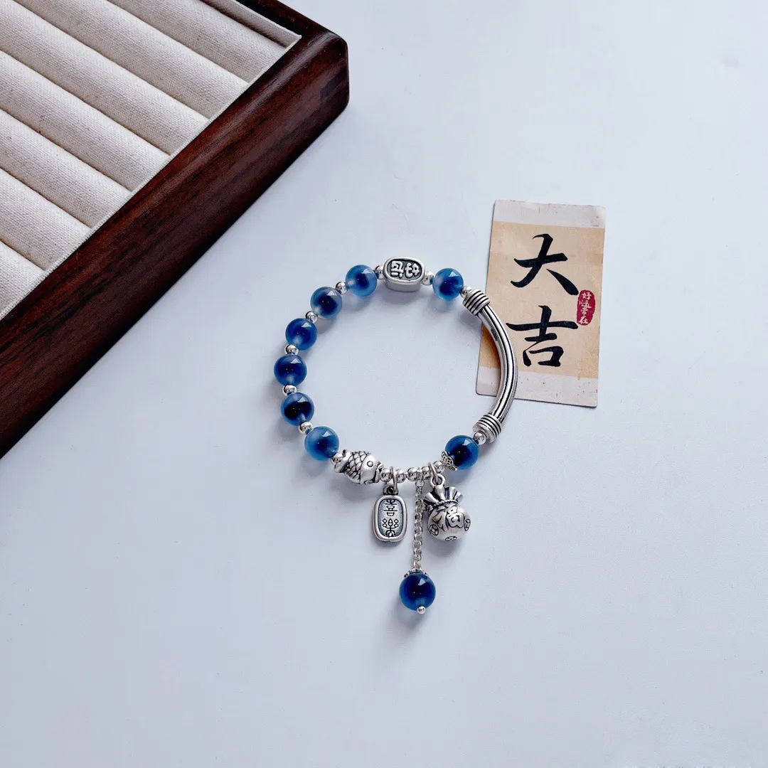 Close-up view of handmade blue agate stones and silver lucky bag charm details on bracelet.