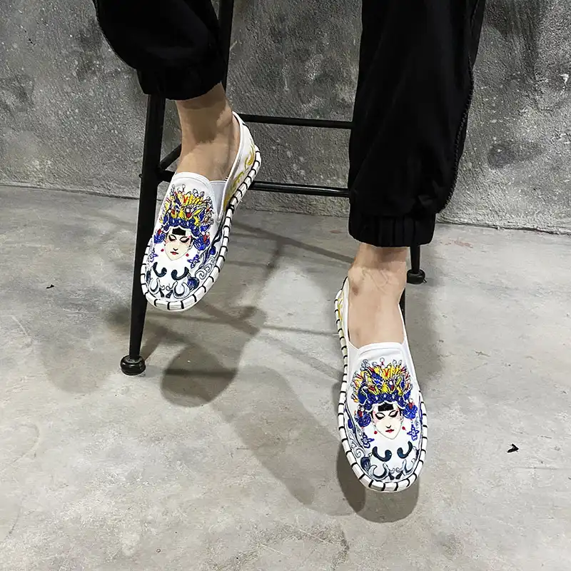 Pair of Old Beijing style shoes on white background displaying ethnic patterns and flat sole.