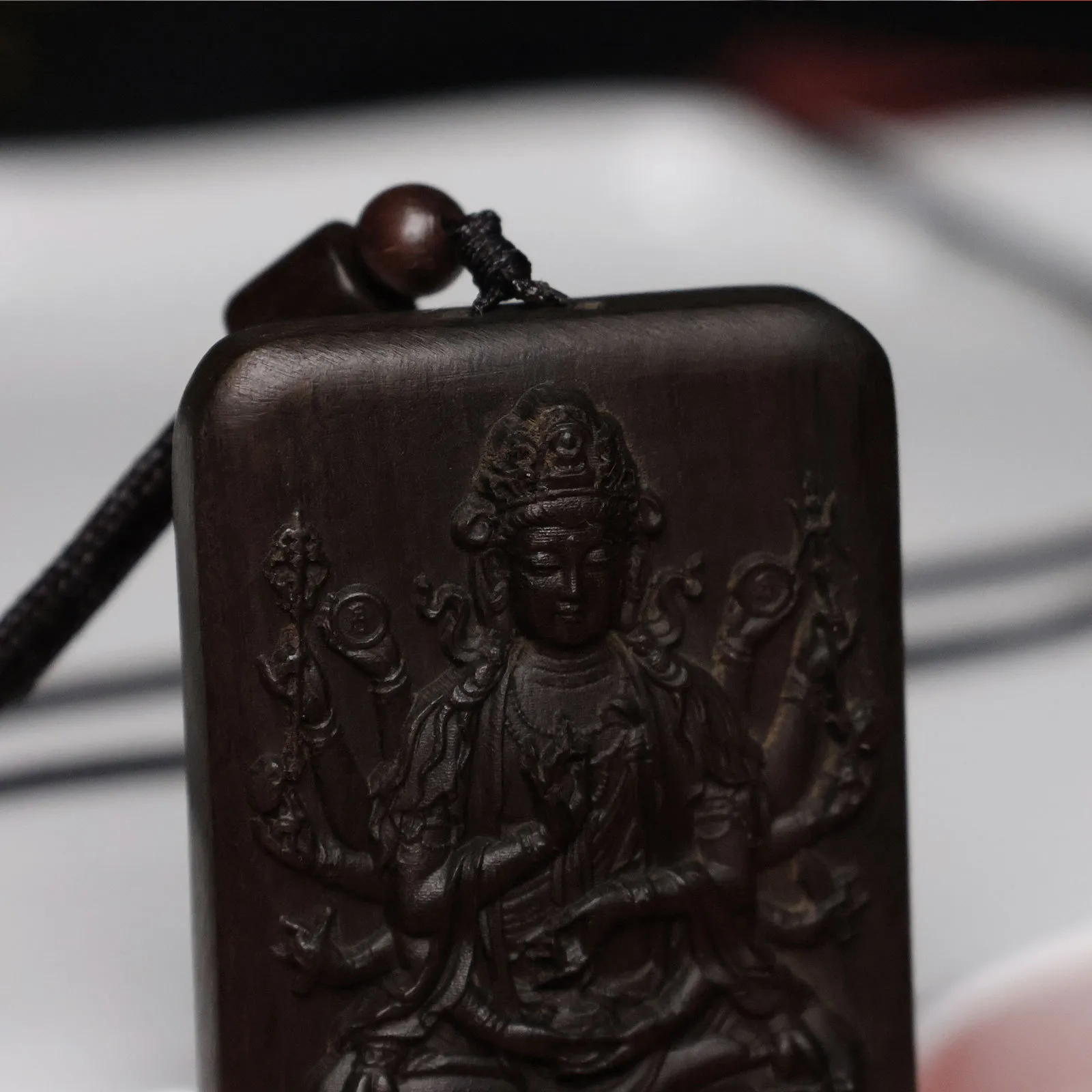 Close-up natural agarwood wood grain texture on carved Thousand Hand Guanyin pendant detail.