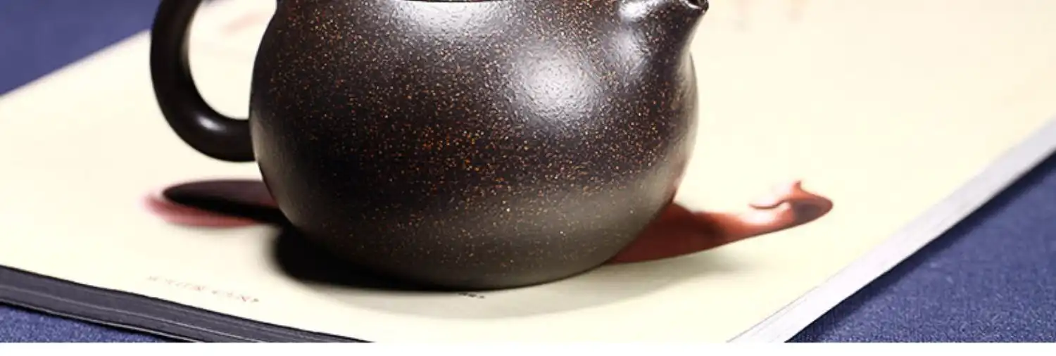 Half handmade teapot spout and handle detail showing smooth black gold sand surface and ergonomics.