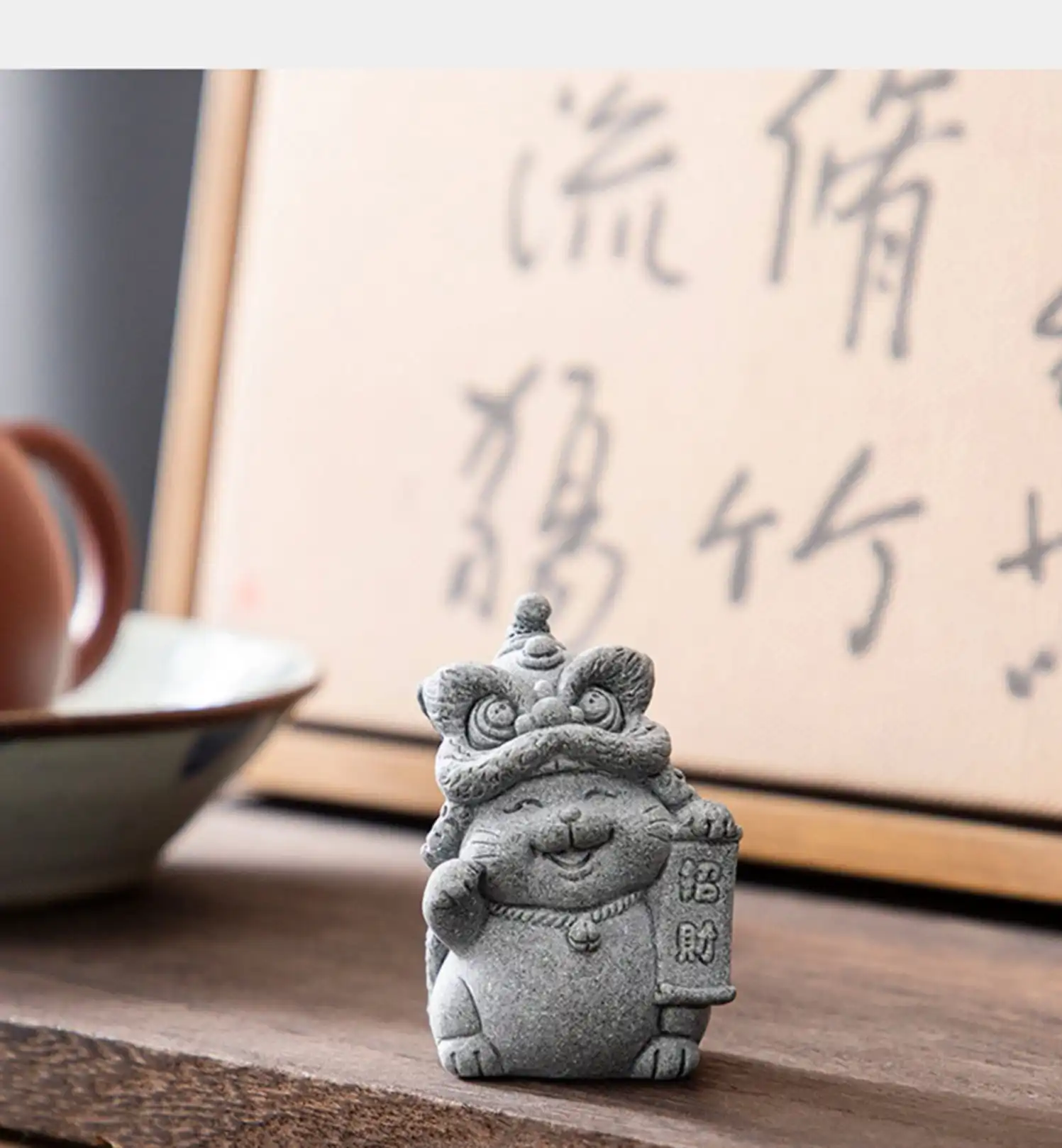 Desktop decoration setup with stone cat tea pet among office supplies and plants.
