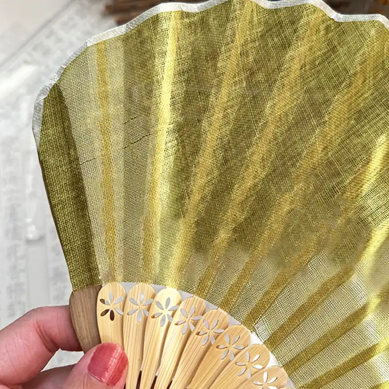 Japanese shell shaped silk folding fan opened displaying curved bamboo ribs and elegant pendant detail.