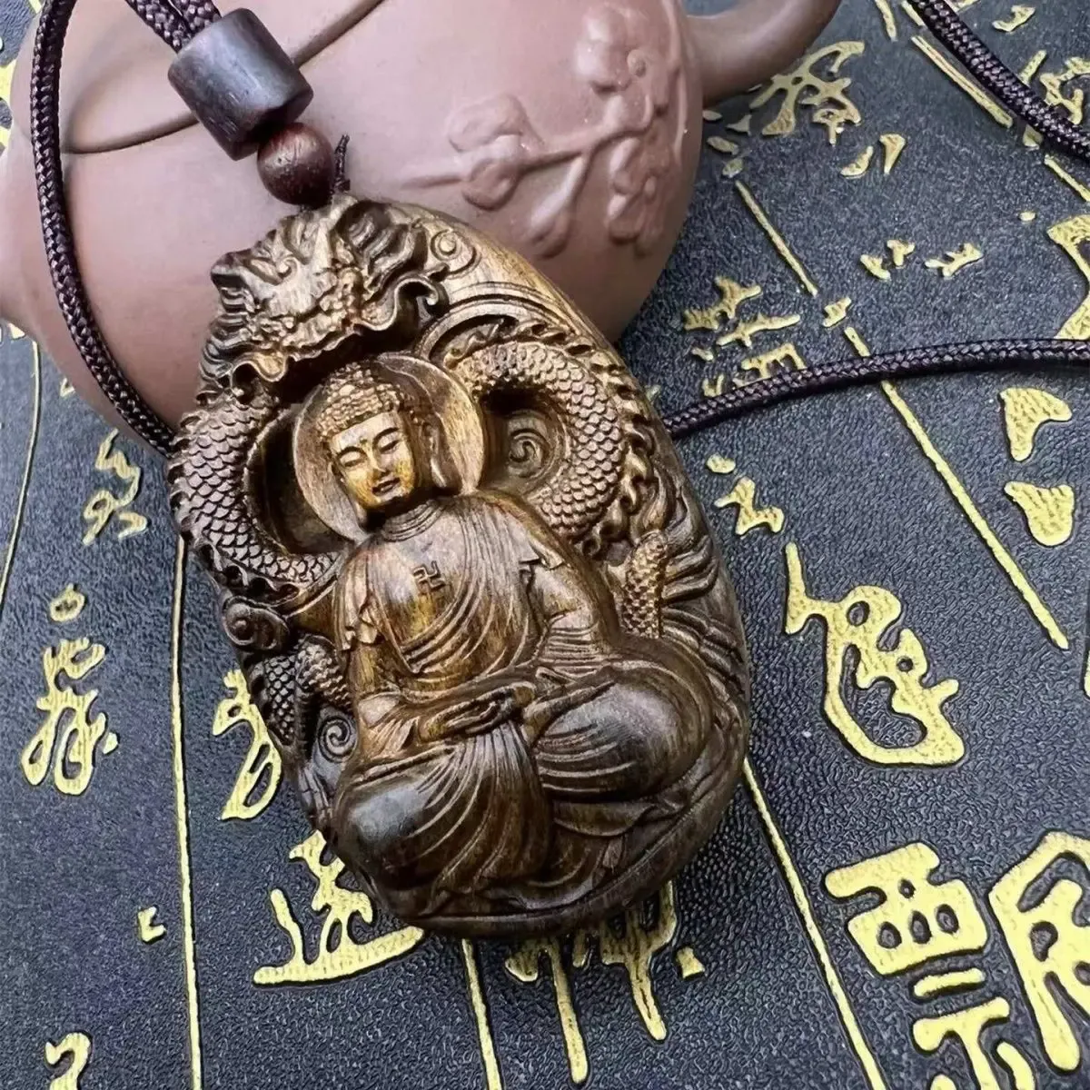 Hands holding sandalwood Tathagata Buddha pendant showing size and carved detail quality.