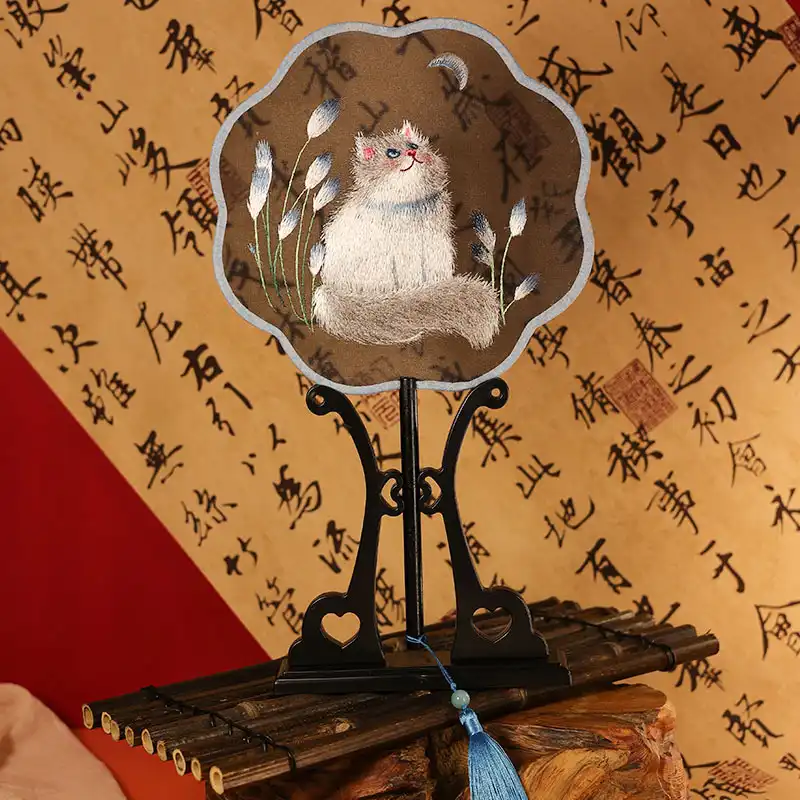 Traditional Chinese hand held fan opened fully showing silk fabric covering and embroidered motifs.