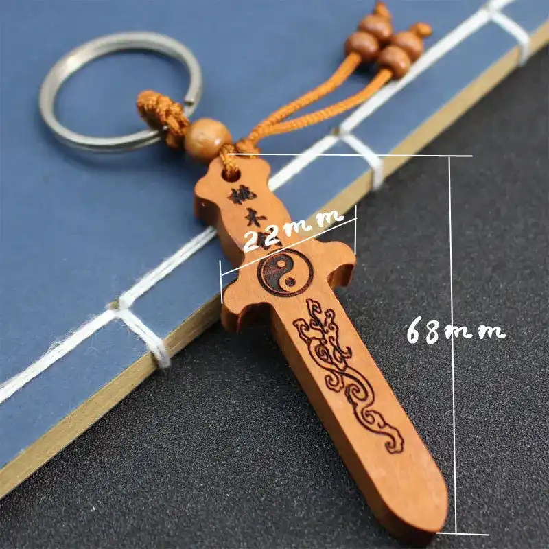Size comparison of peach wood sword keychain with hand showing compact portable dimensions.