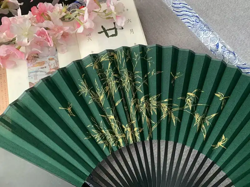 Close-up detail of bamboo forest orchid and lotus flower artwork on silk fan covering.